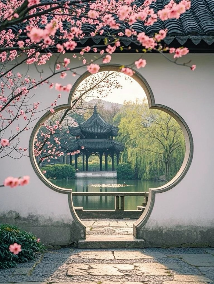 A moon gate framing a lakeside pavilion and spring blossoms in a Suzhou garden